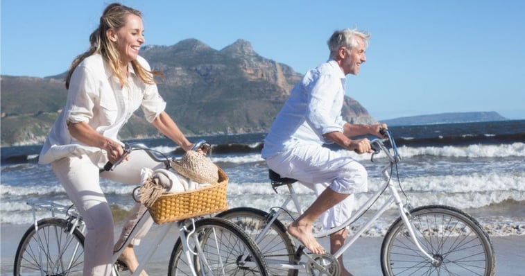 mature couple riding bikes on beach shore not worrying about their hairpiece bonds 