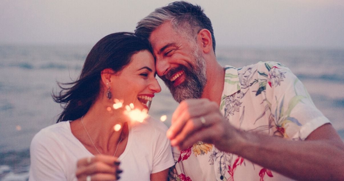 happy mature couple traveling with hairpieces at the beach on a tropical vacation