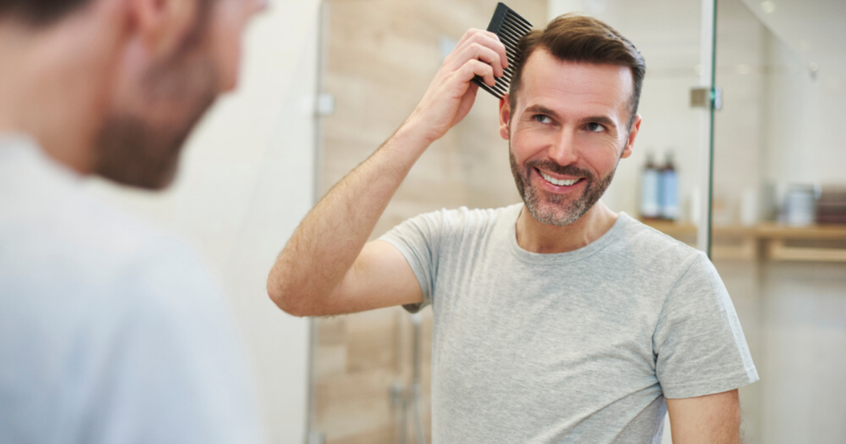 Man combing stock hairpiece in bathroom