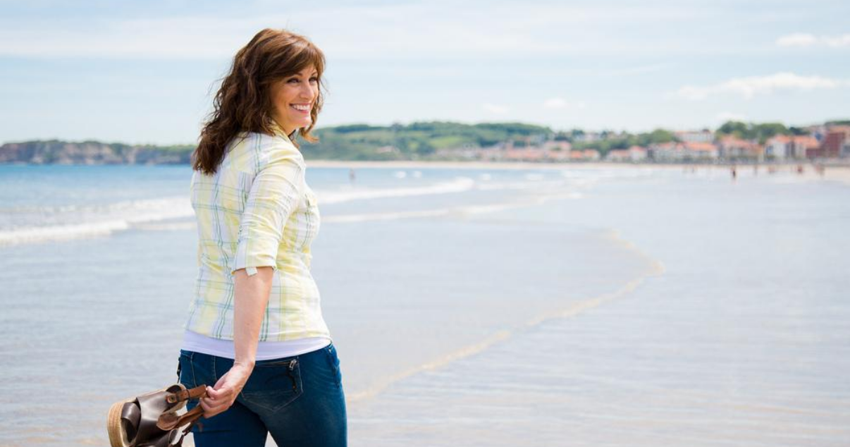 Middle aged woman on beach performing good hair system maintenance