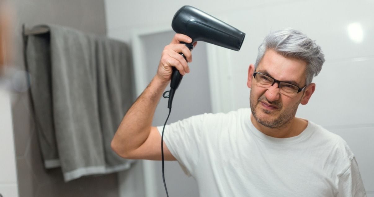 Middle aged man using blow dryer on wig