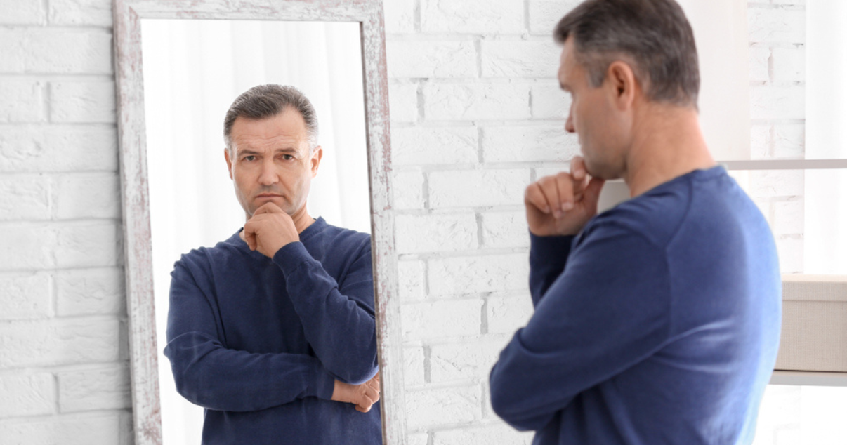 Man looking at mirror wondering if its time to replace his hair system  (1)