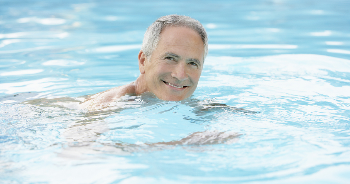 Middle age man swimming without worrying about his hair replacement system getting wet.