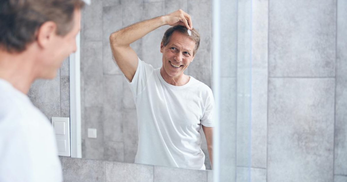Older man doing hair system attachment at home without using hair club