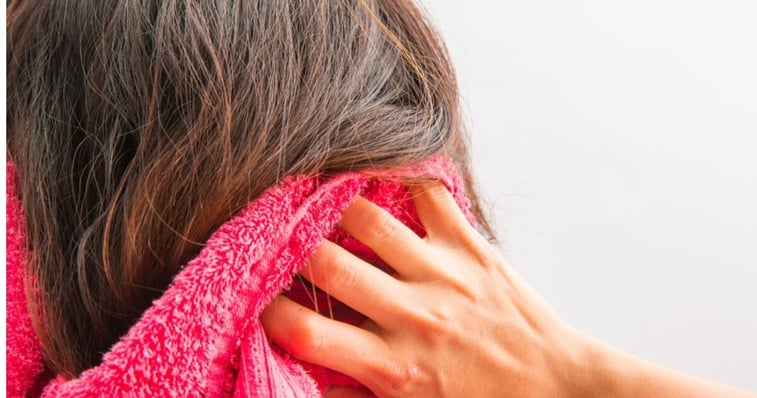 mature brunette woman using a pink towel to dry her hair after washing hair system according to care guidelines 