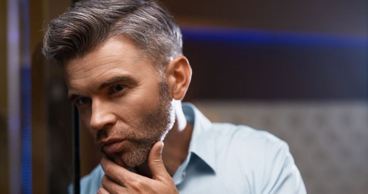 mature man with blue shirt and grey hair admiring hair style after washing hair system and styling it