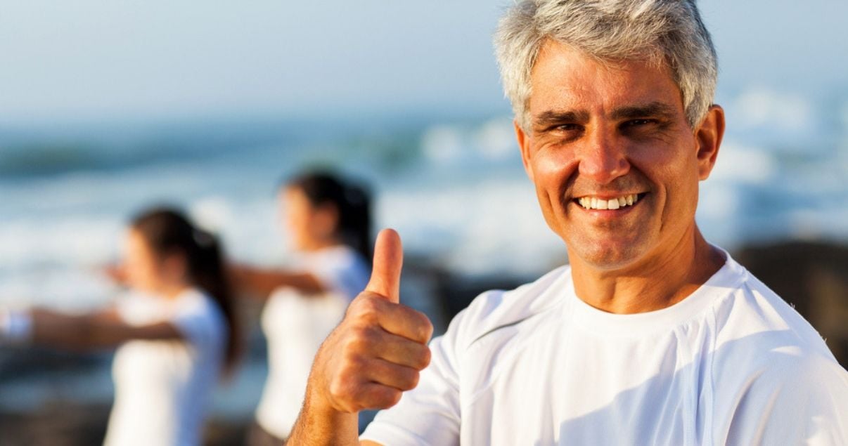 mature man with white shirt walking on the beach approving of his hair system bond after adhesive removal