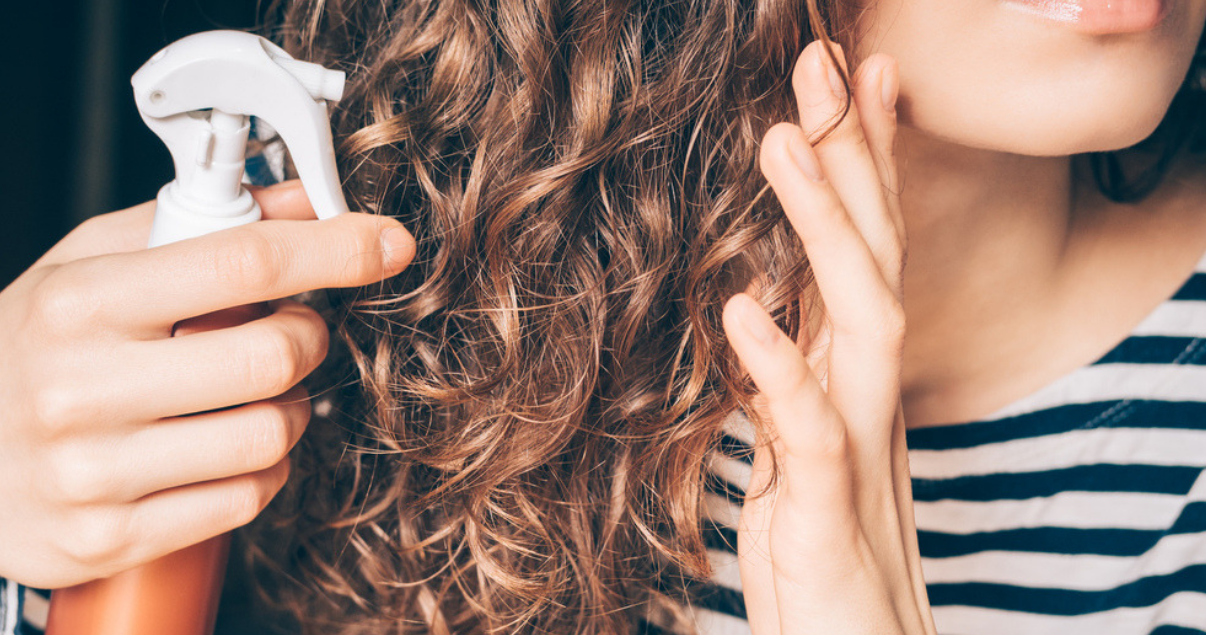Woman applying homemade hair detangler spray on curly brown hair close up