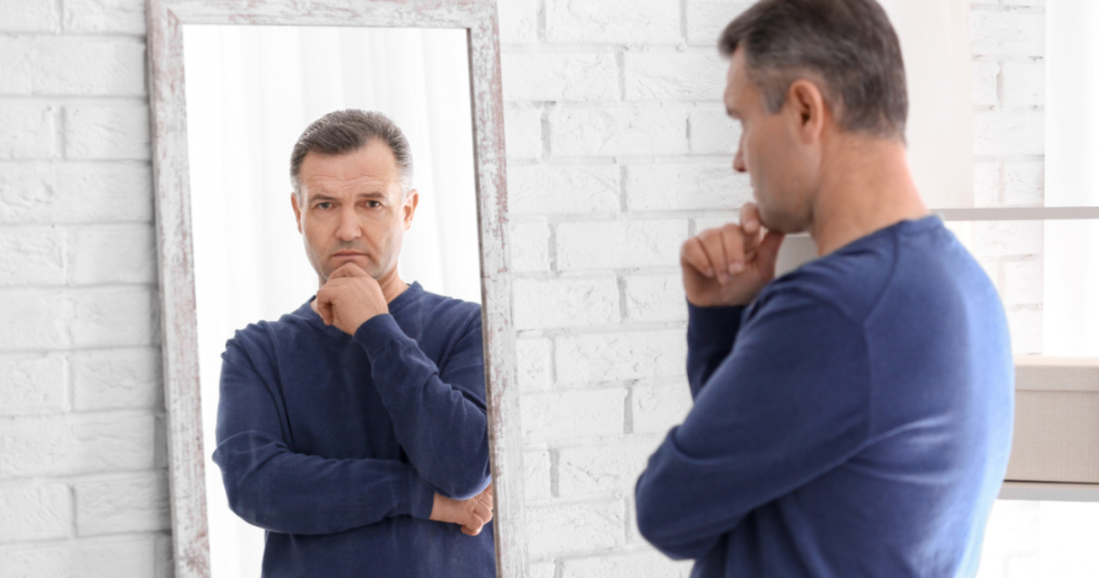 Man looking at mirror wondering if its time to replace his hair system 